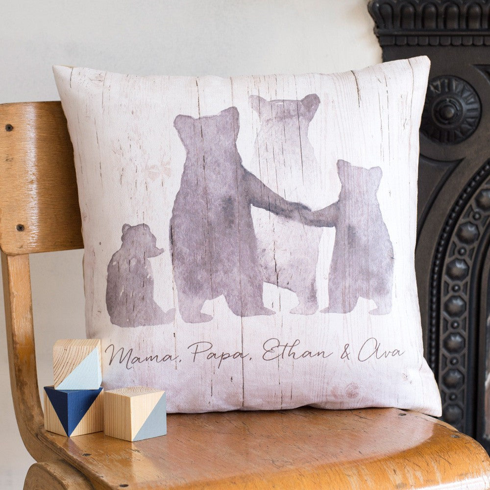 A large, plump cushion sits upon a chair. On the cushion is a family of grey bears, with two parents and two children. Beneath the bears is the text 'Mama, Papa, Ethan & Ava''
