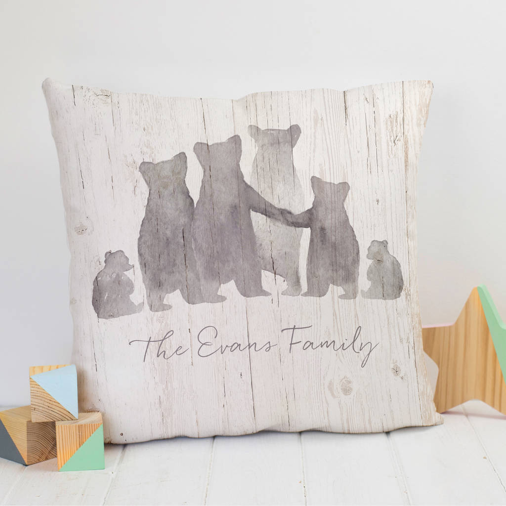 A large, plump cushion sits next to some wooden blocks and a wooden star. On the cushion is a family of six grey bears, with two parents, two young children, an older child and a teenage child. Beneath the bears is the text 'The Evans Family'
