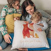 A young couple and their baby are sitting together looking at a cushion that sits on the mothers lap. The baby is leaning over looking at the picture of a family of bears on the front on the front of the cushion. Under the image of the bears is text that reads 'We love you Daddy'