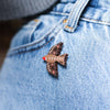 A beautiful wooden pin badge in the shape of a robin, with intricate leaf pattern detailing on the wings and back. It is pinned on to a denim jacket.